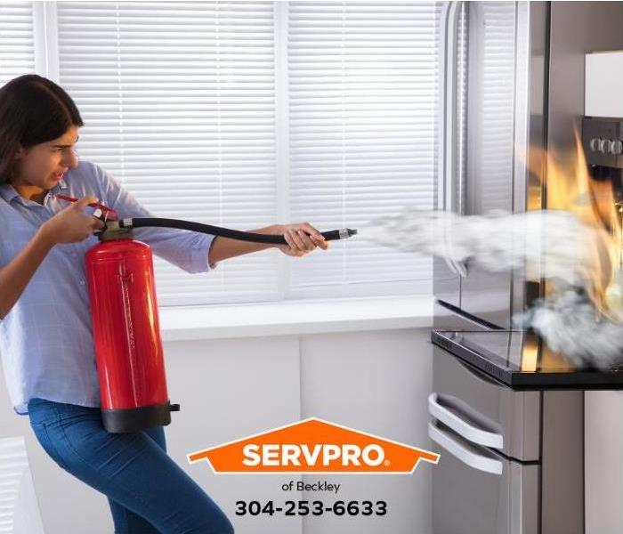 A person uses a portable fire extinguisher to put out an oven fire.